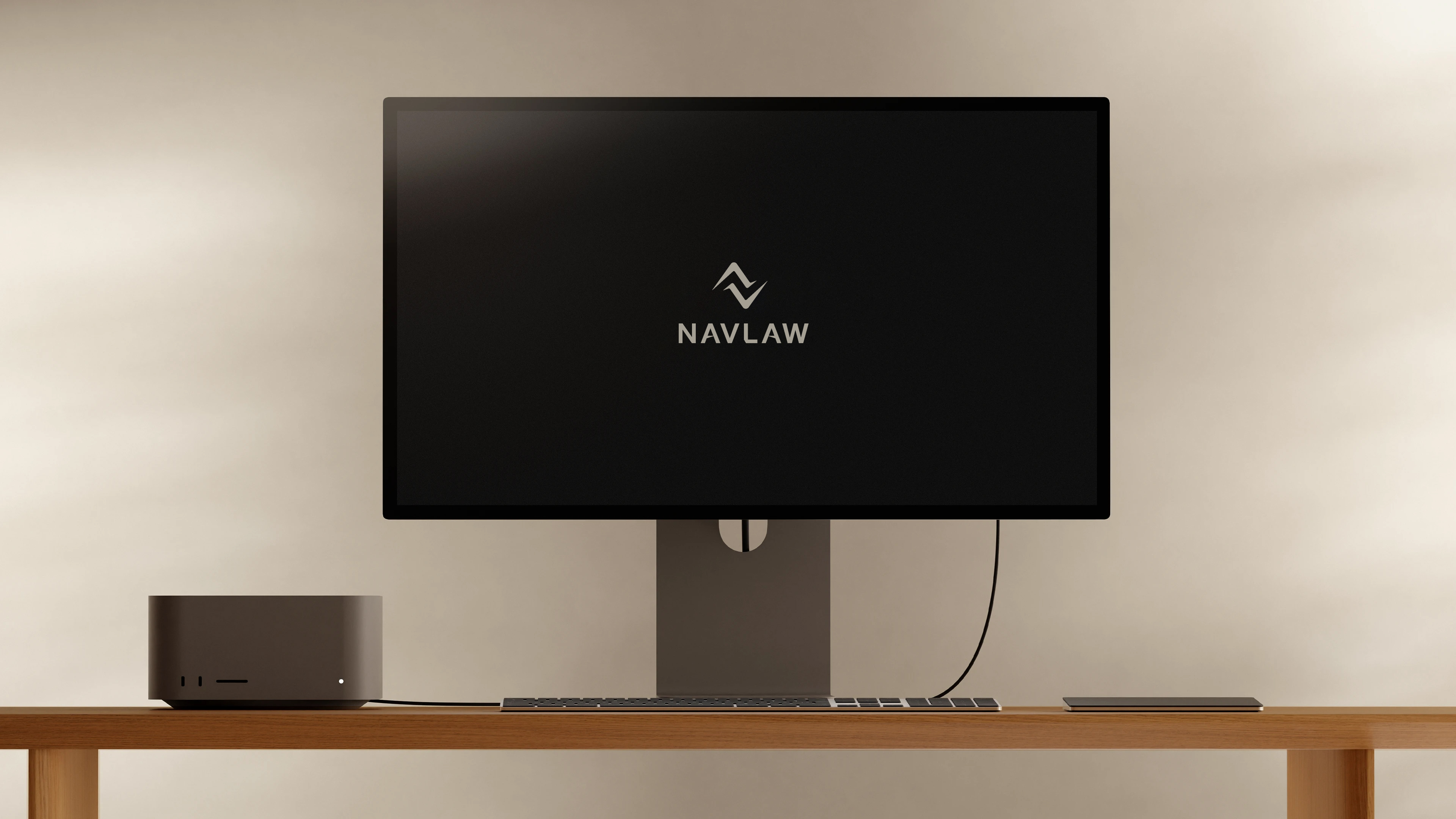 NAVLAW brand identity on Mac Studio desktop display — stacked combination mark in Soft Gold on near-black background, Mac Studio and large display on wooden desk against warm cream wall, showing the law firm brand in a partner office environment