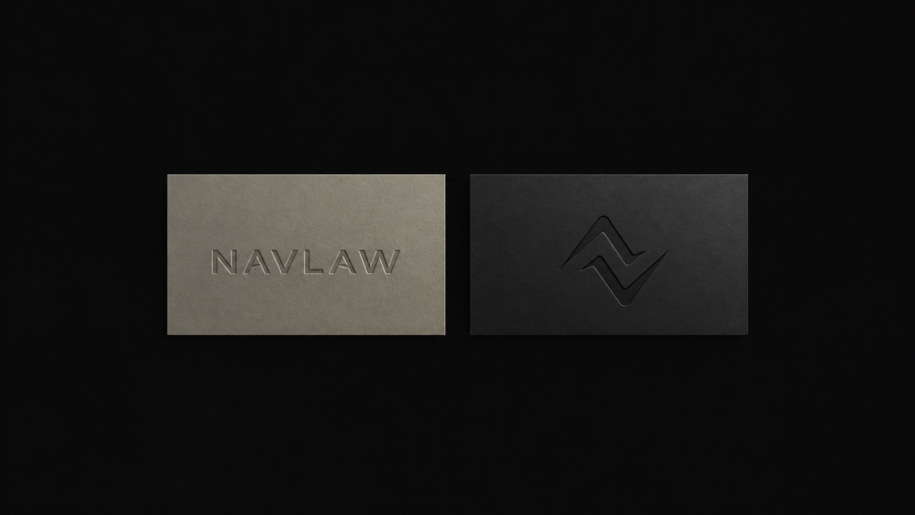 NAVLAW business card detail — the precision of the debossed letterpress impression visible in the soft-gold card stock, no ink, texture and light only
