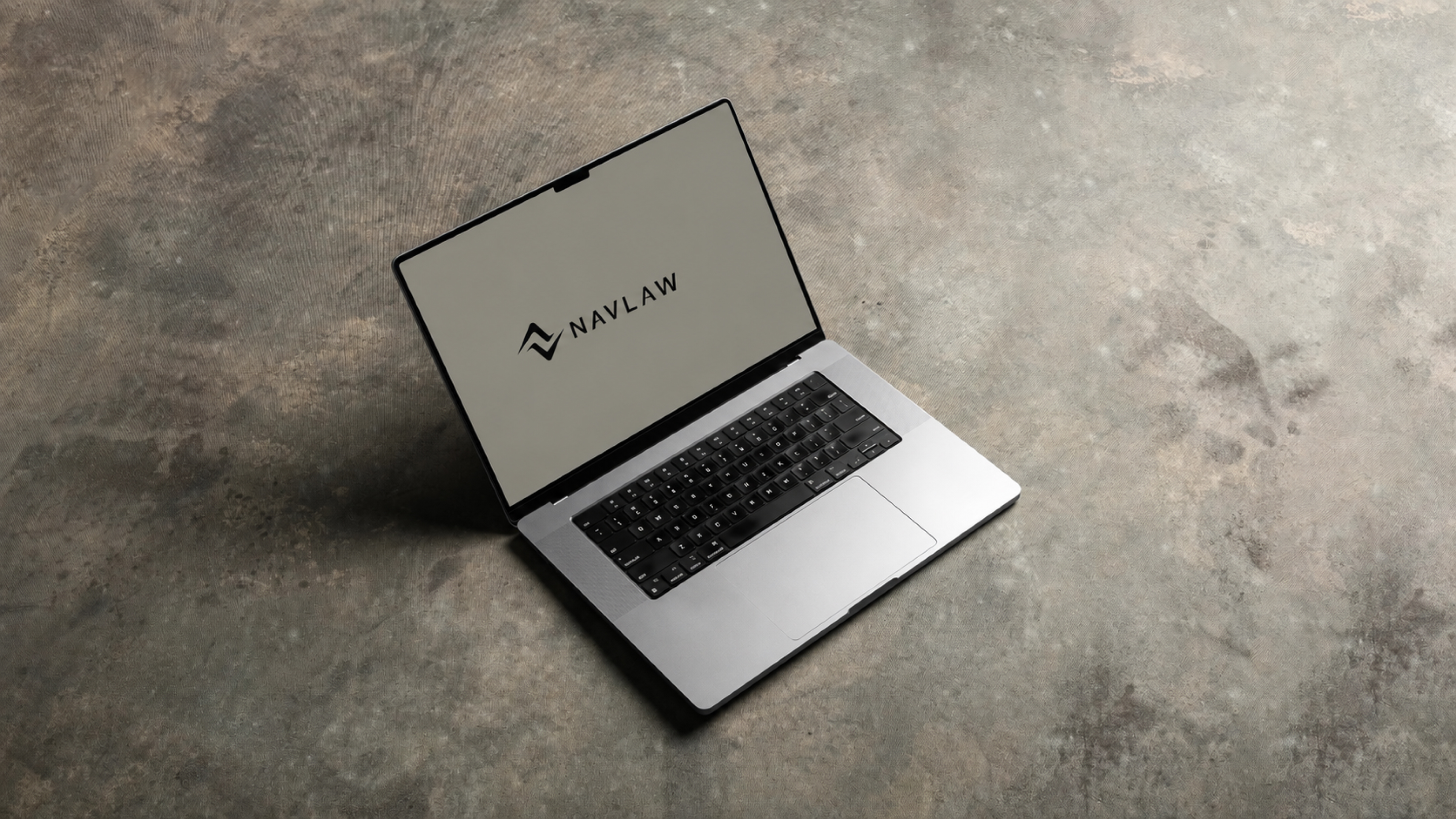 NAVLAW brand identity on MacBook Pro screen — combination mark displayed on Soft Gold background, MacBook photographed on concrete floor surface showing the brand in a modern legal practice environment